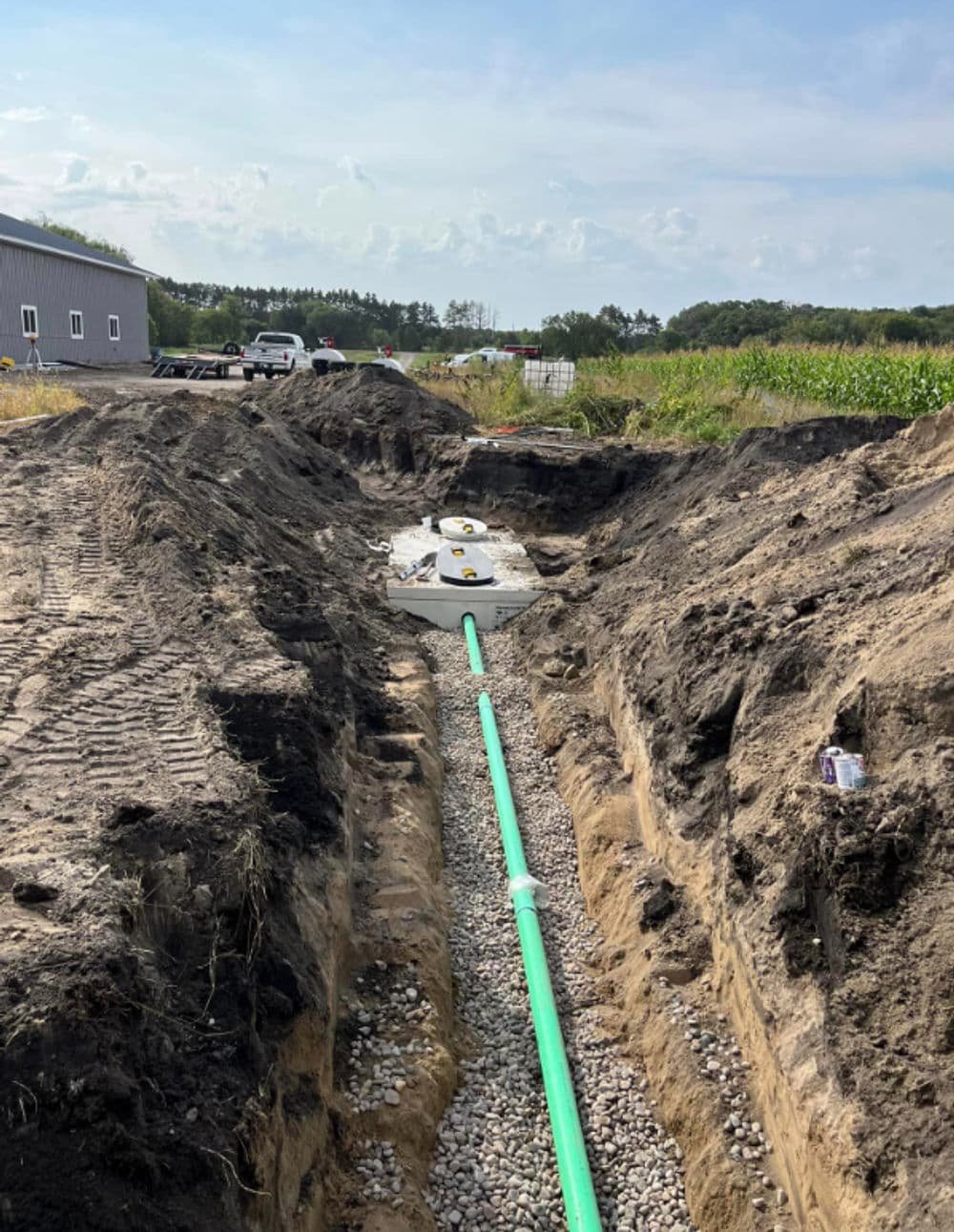 Excavated trench with green piping and gravel for utility installation near a building.