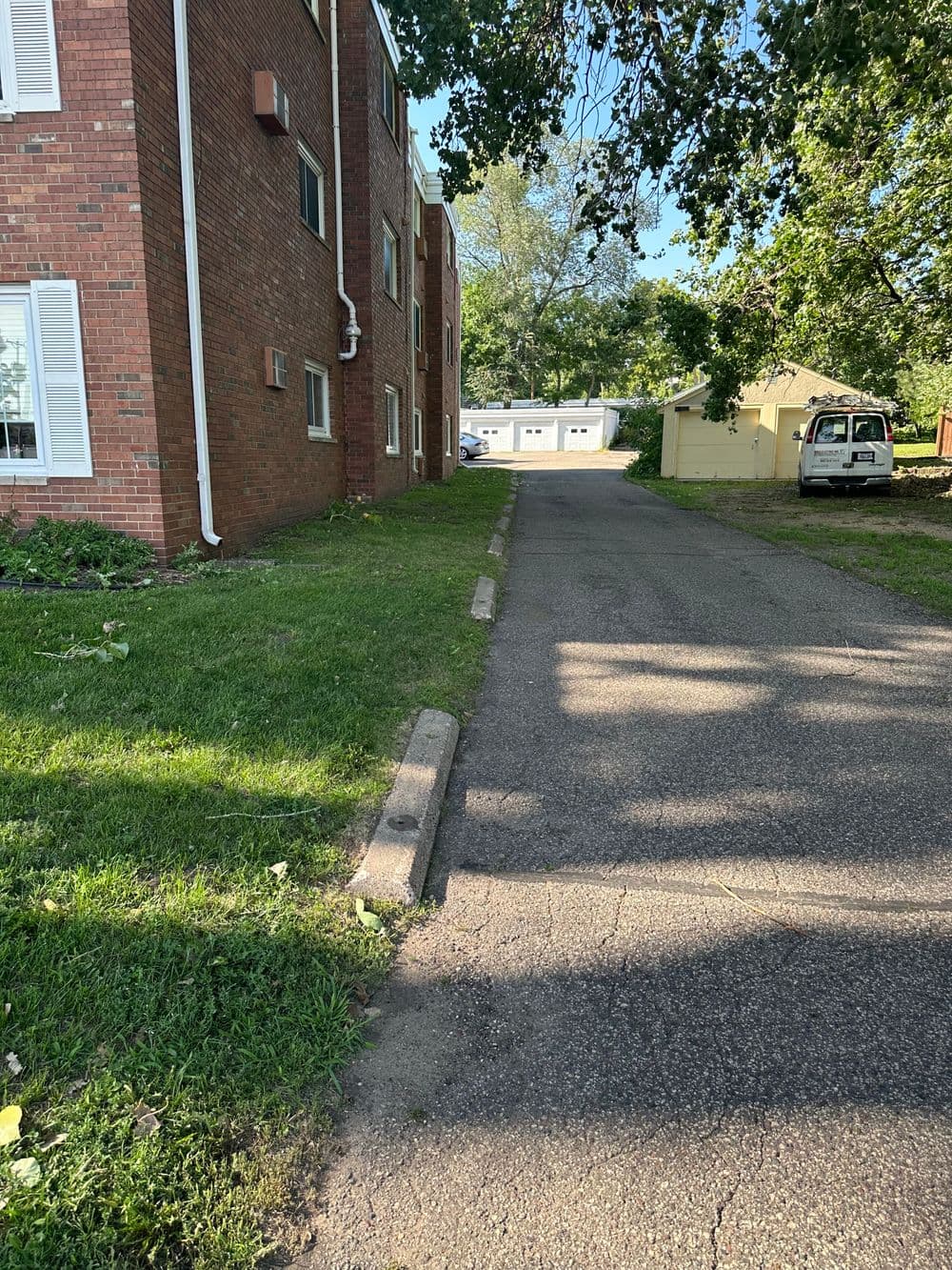 Pathway beside a brick building leading to garages and lush greenery.