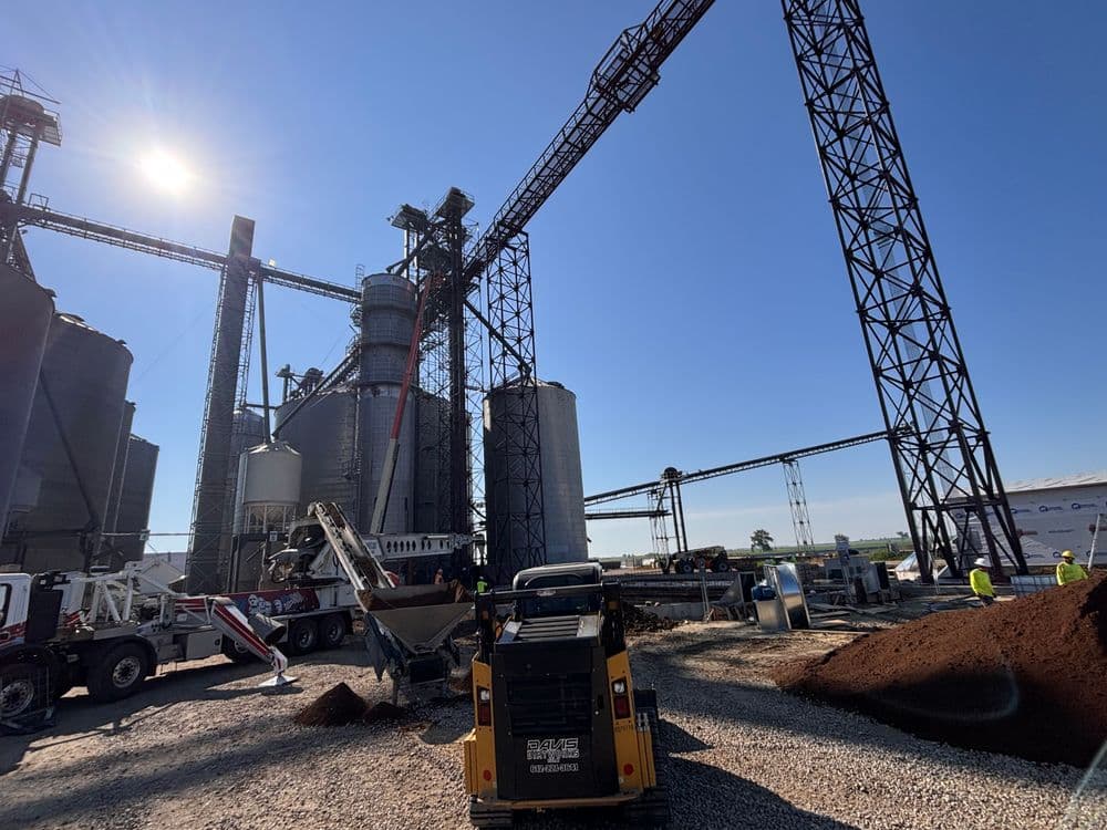 Construction site featuring grain silos, conveyor systems, and machinery under clear blue sky.