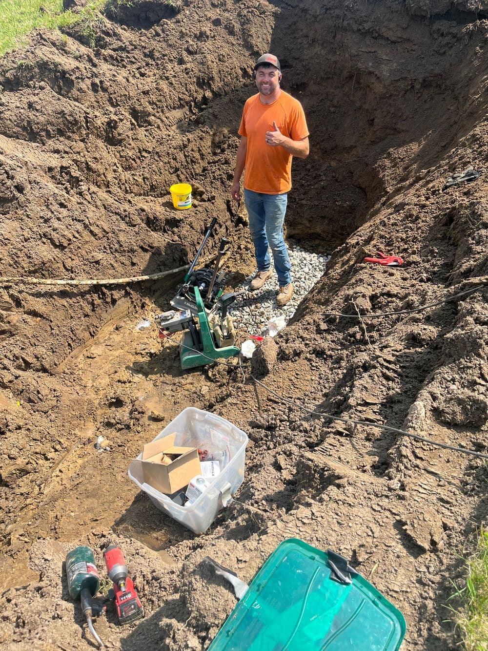 Man in an orange shirt standing in a large excavation site with tools and equipment nearby.