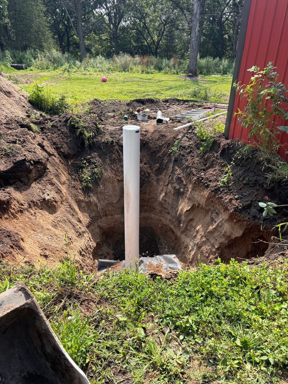 Deep hole for plumbing installation with a white pipe surrounded by dirt and grass.