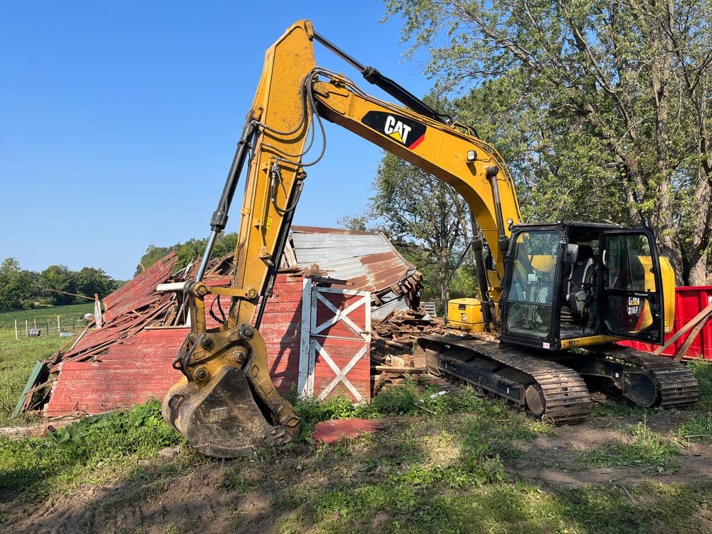 CAT excavator near a collapsed barn, showcasing heavy machinery in rural demolition work.