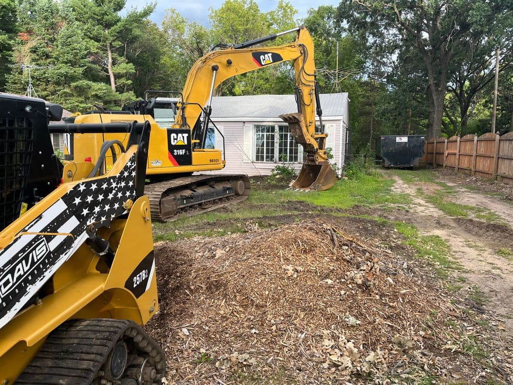 Excavators and skid steers clearing debris in a residential yard renovation project.