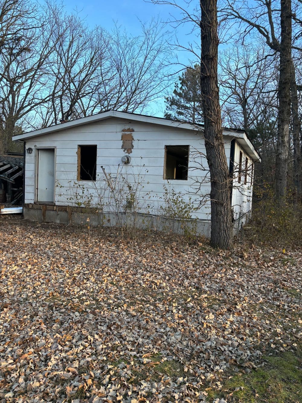 Abandoned house with broken windows surrounded by autumn leaves and trees.